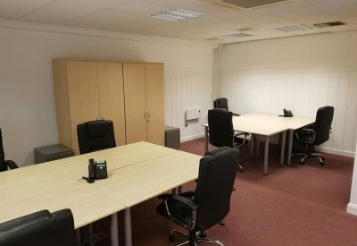 Spacious office suite with multiple light wood desks and black ergonomic chairs.