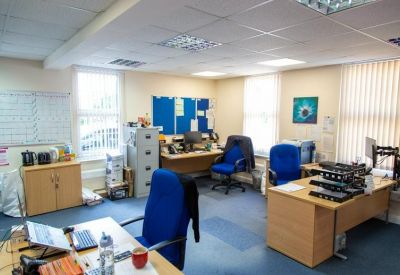 Furnished office space with wooden desks, blue chairs, and natural light from windows.