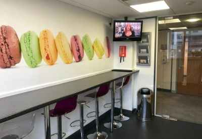 Office breakout area with a long breakfast bar, colorful macaron wall mural, and tall purple stools.
