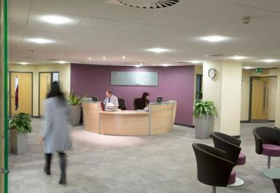 Spacious office lobby with a curved wooden reception desk, purple feature wall, and green potted plants.