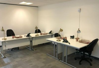 Private office suite with two white desks, black rolling chairs, and brass desk lamps.