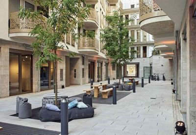 Modern outdoor courtyard with wooden picnic tables, bean bags, and young trees.