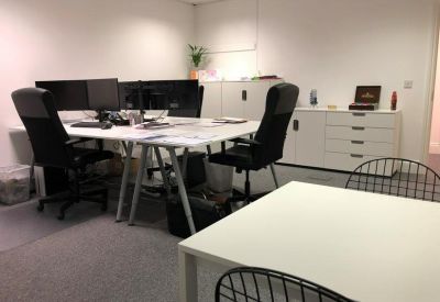 Bright office space with white desks, black ergonomic chairs, and a plant.