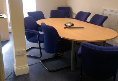 Meeting room with an oval wooden table and blue chairs under a sloped ceiling.
