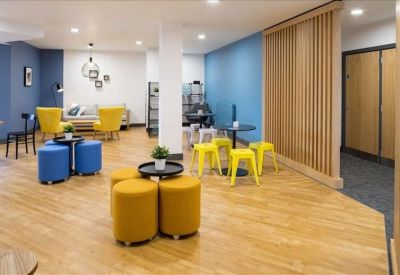 Bright communal lounge featuring vibrant yellow armchairs, blue ottomans, and a feature blue wall.