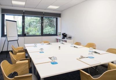 Modern meeting room with a white square table, wooden chairs, and a whiteboard.