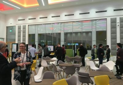 Lively communal hub with people, yellow seating, and artistic wall panels.
