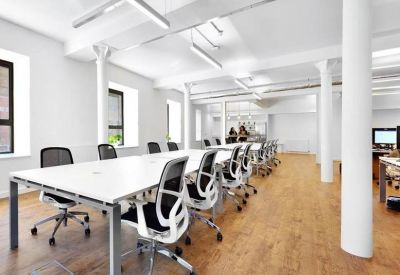 Long white communal desk with ergonomic black mesh chairs in a bright, airy office space.