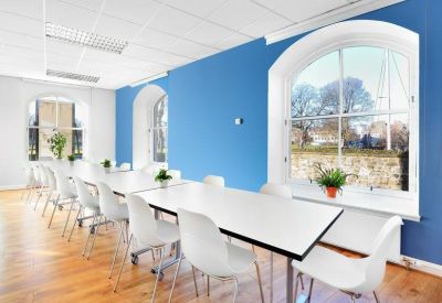 Meeting room with white tables and chairs set against a bright blue feature wall with arched windows.