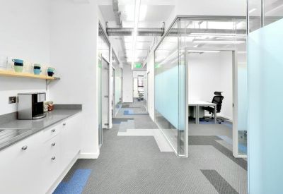 Bright office corridor with a kitchen area and glass-walled private offices.
