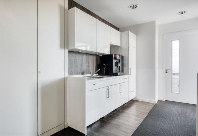 Minimalist white kitchen and break area with a modern coffee machine and integrated sink.