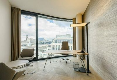Sunlit private office with a light wood desk, ergonomic chair, and floor-to-ceiling city views.