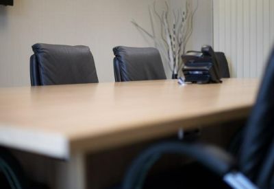 Bright boardroom featuring a light wood table and black leather chairs.