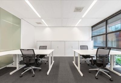 Bright open-plan office with white desks and black mesh ergonomic chairs.