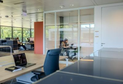 Glass-enclosed office with computer workstations and greenery outside.