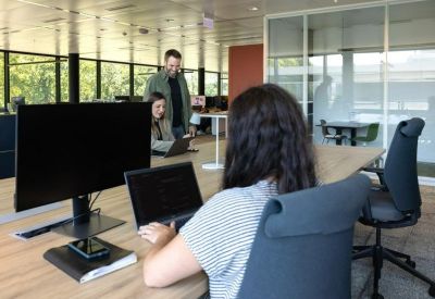 Open office space with computers and a man standing by a desk.