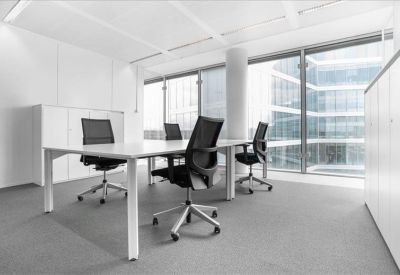 Bright open-plan office with white desks and black ergonomic chairs.