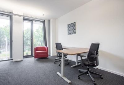 Bright private office featuring a wooden desk and a red armchair by a tall window.