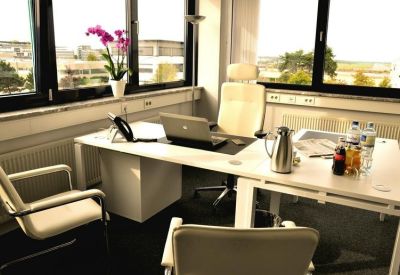 Private office with a large desk, laptop, orchid, and views through floor-to-ceiling windows.