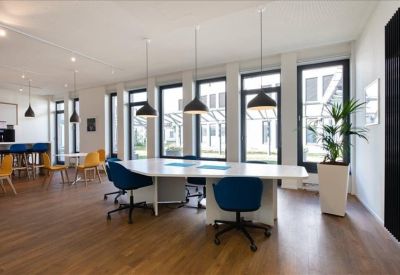 Large open-plan office with a white island desk, blue chairs, and expansive windows.