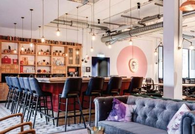 Spacious communal lounge featuring a bar with high stools, leather sofas, and industrial lighting.