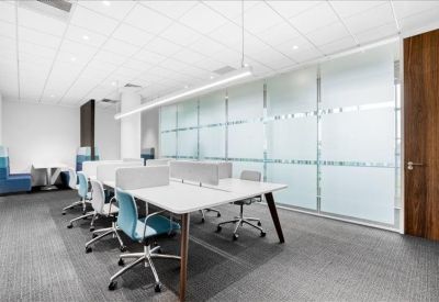 Modern open-plan office with white desks and frosted glass partitions.