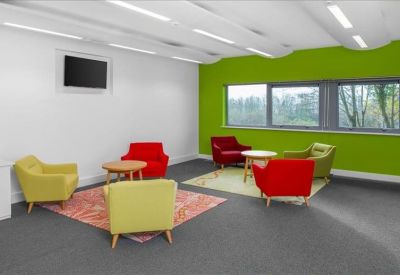 Bright breakout area with colourful red, yellow, and green armchairs on a grey carpet.