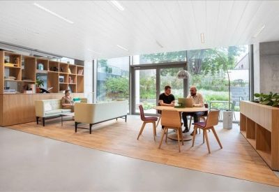 Modern lounge area with light wood shelving, white sofas, and people working at a round wooden table.