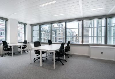 Spacious open-plan office with white desks, black chairs, and large windows overlooking the street.