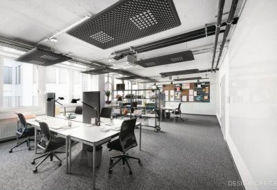 Bright open-plan workspace with multiple desks, black task chairs, and acoustic ceiling panels.