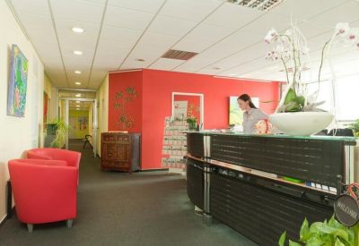 Modern reception area with a black desk, bright red accent wall, and red lounge chairs.