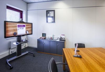 Small meeting room with a wooden table and a wall-mounted video conferencing screen.