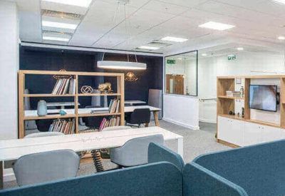 Modern coworking space with white communal tables, wooden shelving, and teal privacy dividers.