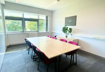 Private meeting room with a light wood table and bright pink chairs.
