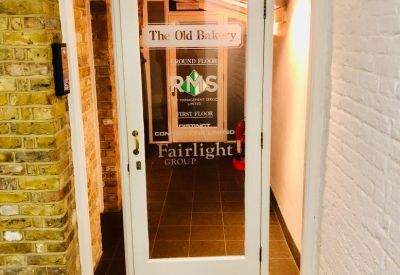 Glass entrance door featuring The Old Bakery signage set within a characterful brick archway.