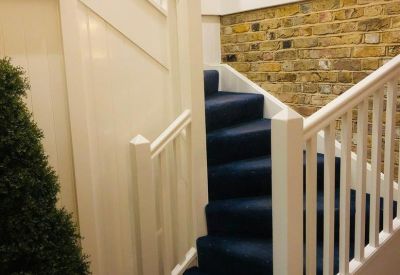 Modern internal staircase with blue carpeting, white railings, and an exposed brick feature wall.