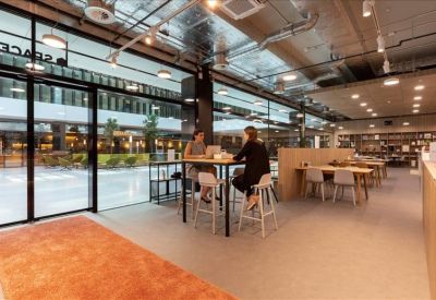 Bright coworking area with high-top tables, glass walls, and an orange rug.