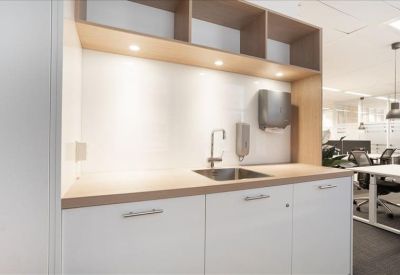Clean, minimalist office kitchenette area with white cabinetry, a light wood countertop, and built-in shelving.