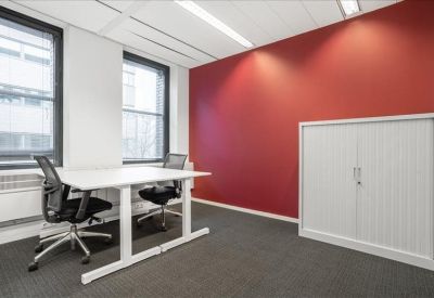 Modern two-person private office featuring a bold red accent wall and white height-adjustable desks.
