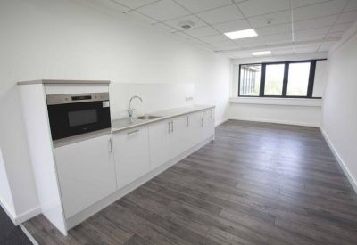 Bright communal kitchenette area with white cabinetry, wood-effect flooring, and integrated microwave.