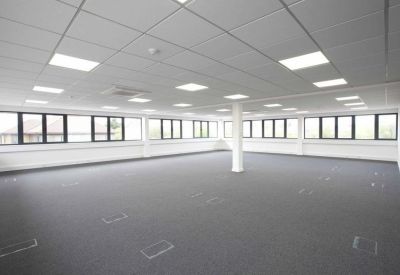Spacious open-plan office space featuring a suspended grid ceiling and large perimeter windows.