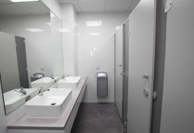 Clean and modern communal restroom facility with multiple white sinks and private cubicles.