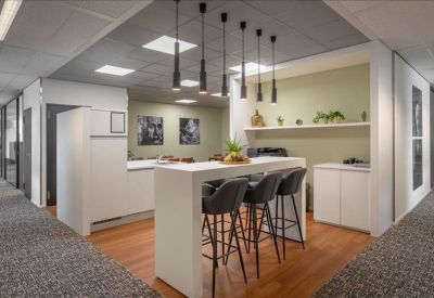 Modern communal kitchen area with a high white breakfast bar, bar stools, and warm wood flooring.