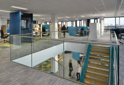 Modern multi-level office interior with glass railings and a central wooden staircase.