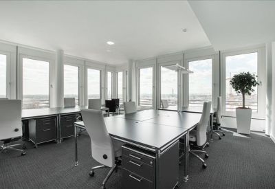 Spacious open-plan office area with several black desks and large windows.