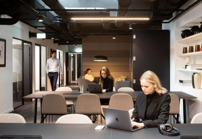 Open-plan workspace with professionals working at long black tables with comfortable seating.