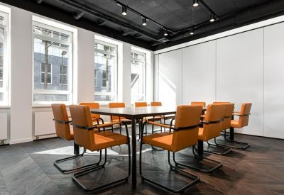 Minimalist boardroom with orange chairs and large windows providing natural light.