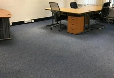 Private office space with blue carpeting and a large L-shaped wooden desk.
