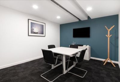 Private meeting room with four black chairs, a teal feature wall, and a wall-mounted TV.