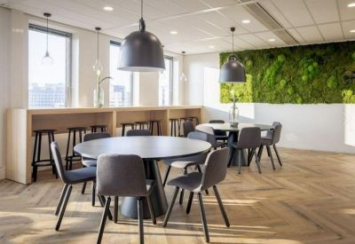 Communal break area with round tables, grey chairs, and a lush green plant wall.